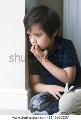 Portrait of young boy biting his finger nails with thinking face,Kid siting with teddy bear and looking out with curiouse face,Childhood and family concept, emotional child, portrait indoor 