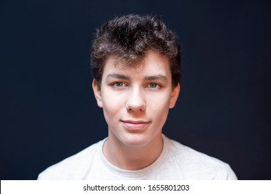 Portrait Of Young Boy With Dark Hair On Dark Background With A Sincere Smile.  A Teenager Has Curly Hair And Beautiful Eyes