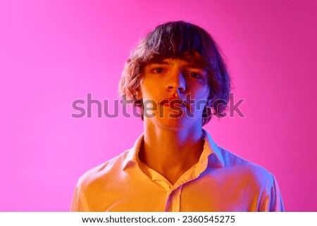 Portrait of young boy looking at camera with calm emotionless face against pink studio background in neon lights. Concept of human emotions, facial expression, youth, lifestyle. Ad Stock photo © 