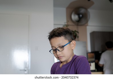 Portrait of young boy wearing glasses looking down at home. Low angle view.