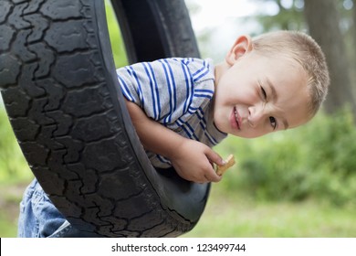 Portrait of a young boy winking while swinging on tire