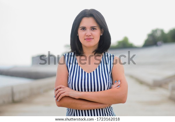 Portrait of\
a young brunette girl of European descent, in a striped dress.\
Portrait of a young brunette walking along the embankment of the\
sea or river in the summer on a sunny hot\
day