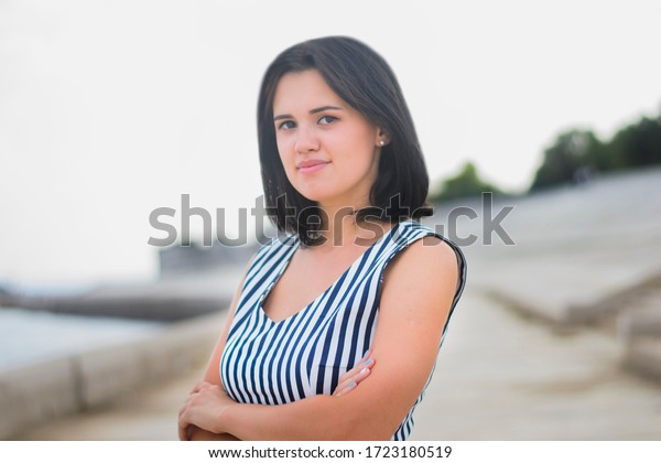 Portrait\
of a young brunette girl of European descent, in a striped dress.\
Portrait of a young brunette walking along the embankment of the\
sea or river in the summer on a sunny hot\
day\

