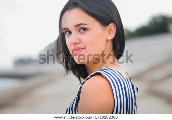 Portrait\
of a young brunette girl of European descent, in a striped dress.\
Portrait of a young brunette walking along the embankment of the\
sea or river in the summer on a sunny hot day\
