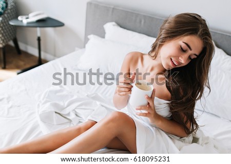 Portrait Young Brunette Girl With Naughty Legs And Shoulders On White Bed She Holds Cup Portrait Young Brunette Girl With Naughty Legs And Shoulders On White Bed She Holds Cup