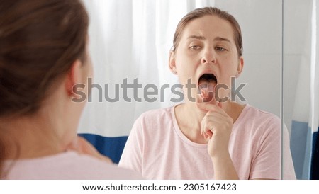 Portrait of young brunette woman checking her tongue for plaque and microbes while looking in mirror.