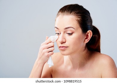 Portrait Of A Young Brunette Woman Cleaning Her Face With Wet Wipes. Girl Is Removing Make-up With Facial Tissues Isolated On Grey Background. Beauty Skin Care Concept.