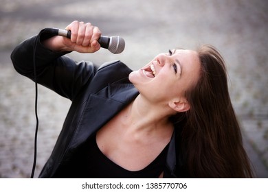 Portrait Of Young Brunette Woman Singing With Microphone Outdoors