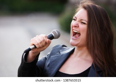 Portrait Of Young Brunette Woman Singing With Microphone Outdoors