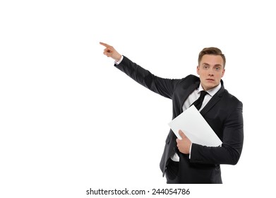 Portrait Of A Young Business Man Holding Magazine And Pointing To The Left. Concept Of Showing The Right Direction In Business. Isolated On White Background.