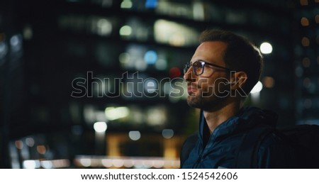 Portrait of an young business man is wearing handsfree earphones in the evening in a city center.