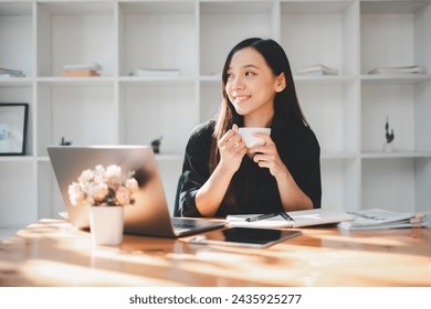 Portrait of young business woman drinking coffee at desk with laptop in office. - Powered by Shutterstock