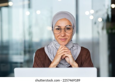 Portrait of young business woman in hijab, muslim woman close up smiling and looking at camera, arab woman in glasses successful working inside office with laptop. - Powered by Shutterstock