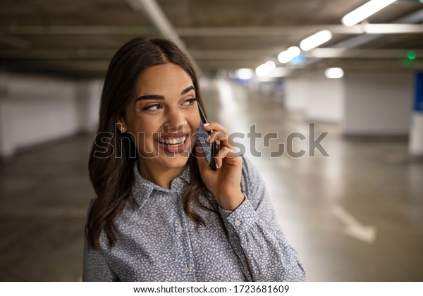 Portrait of young business woman with smart phone\
in the underground car parking of the new residential building.\
Businesswoman in underground garage. Elegant woman using smartphone\
in parking garage