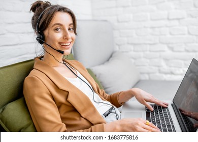 Portrait Of A Young Business Woman Working On Computer, Talking Online Using A Headset While Sitting On The Comfortable Sofa At Home. Concept Of Remote Work From Home