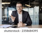 Portrait of a young businessman, a business coach conducts training and online training, professional development. Sitting in the office at the table in front of the camera, gesturing with his hands.