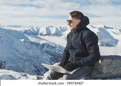 Portrait of young businessman freelancer working on a laptop on top of the world. Winter lanscape in sunny day