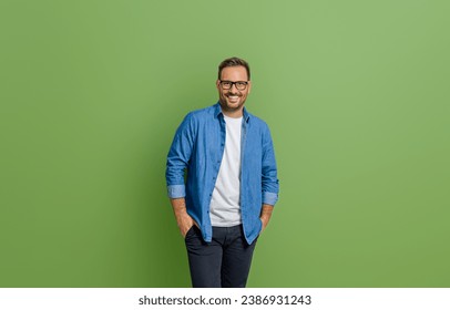 Portrait of young businessman with hands in pockets standing isolated against green background - Powered by Shutterstock