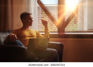 Portrait Of Young Businessman With Laptop At Window Of Living Room In Country House. Workaholic Man In Home Casual Clothes Working On Vacation. Creative Inspiration And Start-up Business. Copy Space