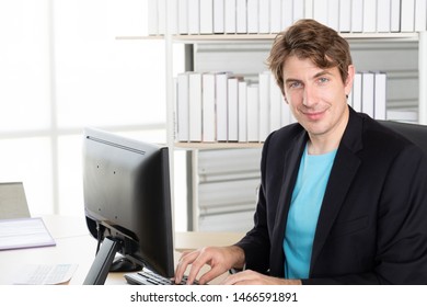 Portrait Of Young Businessman Sitting At Home Office And He Happy Looking Straight At Camera While Use Computer, Or Use Internet Search For Business Online Concept.