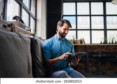 Portrait of young businessman with tablet indoors in office, looking at camera.