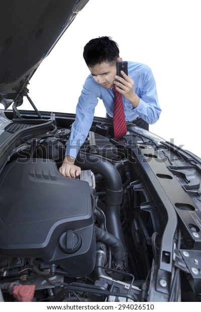 Portrait of young\
businessman talking on the phone while checking the broken machine\
car, isolated on white