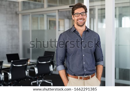 Portrait of young businessman wearing eyeglasses and standing outside conference room. Portrait of happy business man wearing spectacles and looking at camera with copy space. Satisfied proud man.