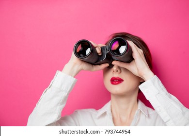 Portrait of young  businesswoman with binoculars on pink background. Concept of looking for new job