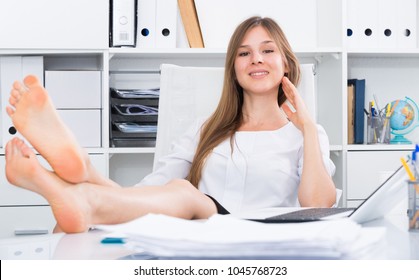 Portrait of young businesswoman relaxing in office with bare feet on desk 