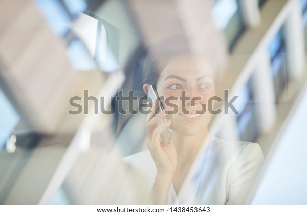 Portrait of young businesswoman\
speaking by smartphone in taxi shot from behind glass, copy\
space