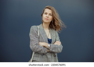 Portrait Of Young Businesswoman Standing With Crossed Arms In Stylish Blazer And Looking With Mistrust On Gray Background. Urban Lifestyle, Entrepreneur, Well Dressed Lady, Successful People.