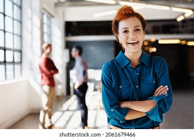 Portrait Of A Young Businesswoman Standing In An Office With Her Colleagues In The Background