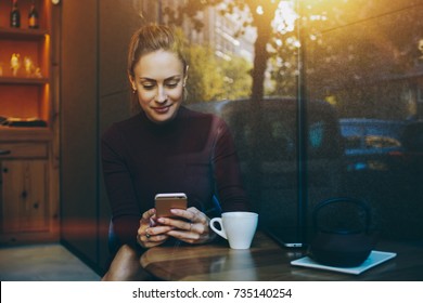 Portrait of young businesswoman use mobile phone while sitting in comfortable coffee shop during work break, charming happy female reading fashion news on cell telephone during breakfast in restaurant - Powered by Shutterstock