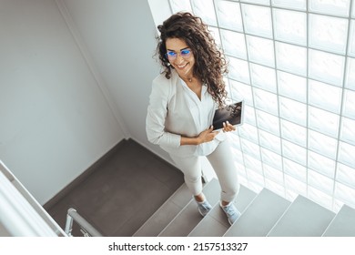 Portrait of a young businesswoman using a digital tablet while walking up a staircase in an office. Businesswoman walking upstairs and using touchpad. Business concept