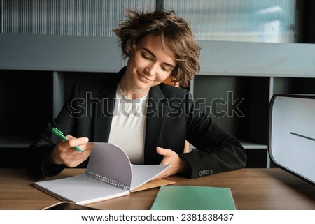 Portrait of young businesswoman working in her office, reading papers, studying documents of case and smiling, sitting in suit, having an interview.