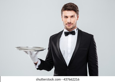Portrait of young butler in tuxedo holding empty tray