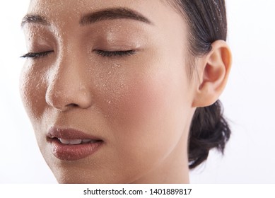 Portrait of a young calm Asian woman having wet face while standing isolated on the white background with closed eyes