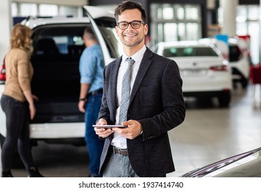 Portrait Of Young Car Salesman At Dealership Salon, Looking At Camera.