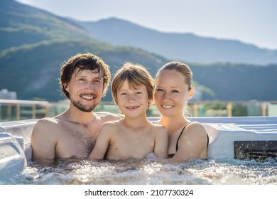 Portrait Of Young Carefree Happy Smiling Happy Family Relaxing At Hot Tub During Enjoying Happy Traveling Moment Vacation. Life Against The Background Of Green Big Mountains