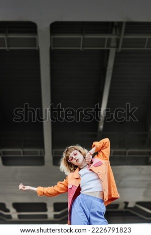 Portrait of young carefree woman wearing street style fashion outdoors and dancing in urban setting