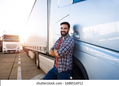 Portrait of young Caucasian bearded trucker with arms crossed standing by his truck vehicle. Transportation service. Truck driver job.
