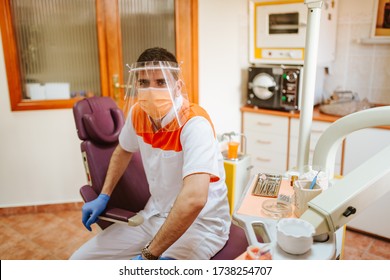 Portrait Of A Young Caucasian Dentist With A Mask And Visor In A Dental Office. COVID - 19 Virus Protection