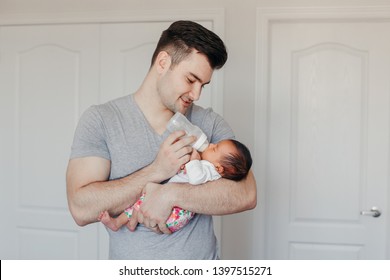 Portrait of young Caucasian father dad feeding Asian Chinese mixed race newborn baby son daughter with milk from bottle. Authentic lifestyle candid real moment. Single dad family life concept. - Powered by Shutterstock