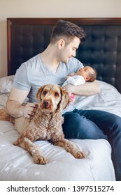 Portrait Of Young Caucasian Father With Mixed Race Asian Chinese Newborn Baby. Dog Pet Lying On Bed. Man Parent Holding Child Daughter Son. Authentic Lifestyle Moment. Single Dad Family Life. 