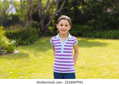 Portrait Of Young Caucasian Girl Wearing Striped T-shirt And Standing In The Garden. Spending Time Alone Outside Concept.