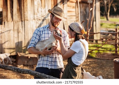 Portrait Of Young Caucasian Happy Farmer Couple Holding A Little Goat In Their Arms. Family Business At Ecological Farm. Healthy Food.Industrial Production Of Goat Milk Dairy Products. Cattle Farming.