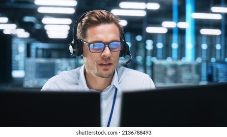 Portrait of a Young Caucasian Male Call Centre Worker Wearing a Phone Headset Talking at the Support Line with Serious Face in a Modern Open Plan Office at Night. Helpline Concept - Shutterstock ID 2136788493