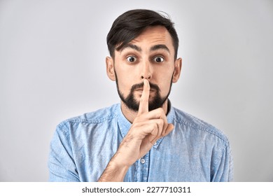 Portrait of young caucasian man covering his mouth with finger isolated on white background. Asks for silence, keep secret, shh gesture