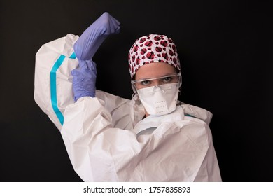 Portrait Of A Young Caucasian Nurse Wearing A Personal Protective Equipment And Posing As A Female Worker Raising Her Arms. Concept Of Female Worker And We Can Do It.