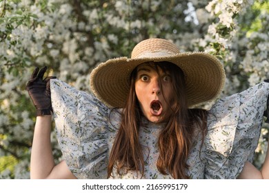 Portrait of young caucasian shocked afraid woman in straw hat looking with staring eyes, having wide open mouth. Hold in her hands the sleeves of dress. Summer vacation concept. Seasonal allergy.